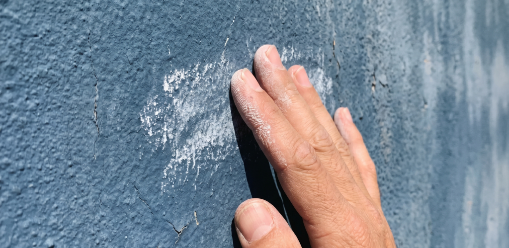 Tangan menyentuh dinding yang menunjukkan ciri cat tembok mengapur dan pudar